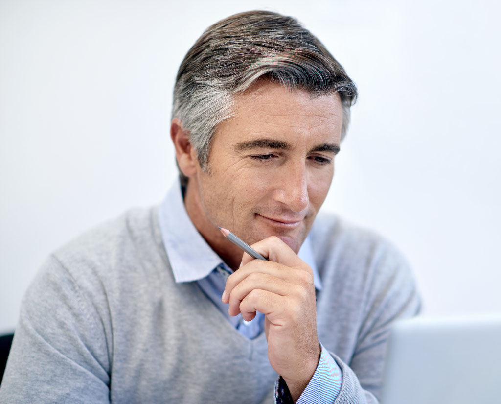 Man looking at computer screen holding his chin with a pencil in his hand and an expression on his face that depicts thinking
