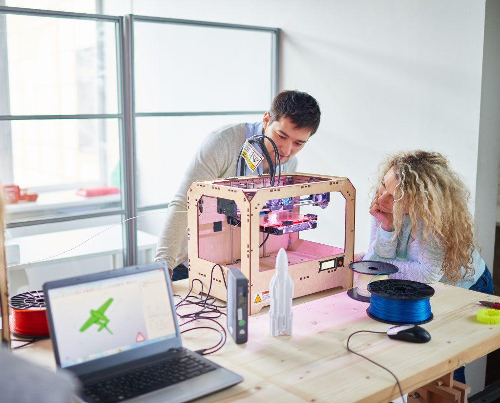 A man and woman look closely at a 3d printer in use.