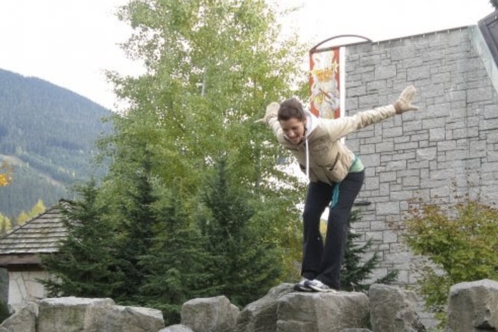 An image of Gina Sparrow about to jump off a rock with trees and mountains in the background.