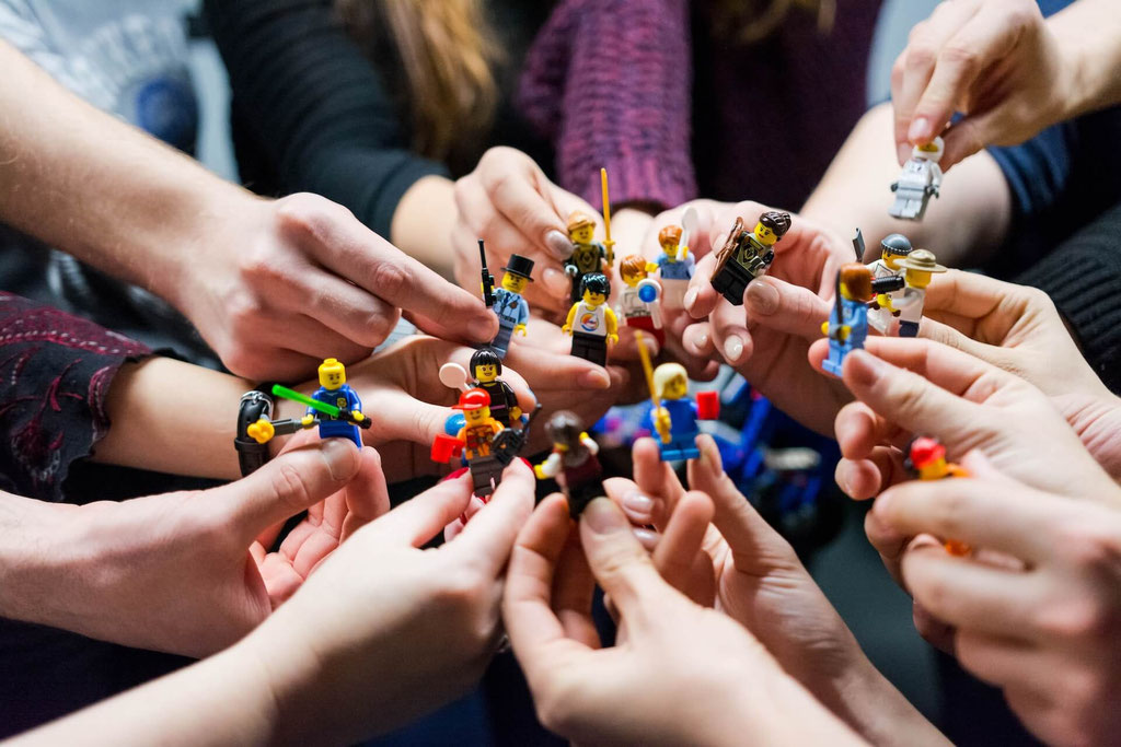 Close up picture of the hands multiple people holding different Lego figurines up to one another in a circle 