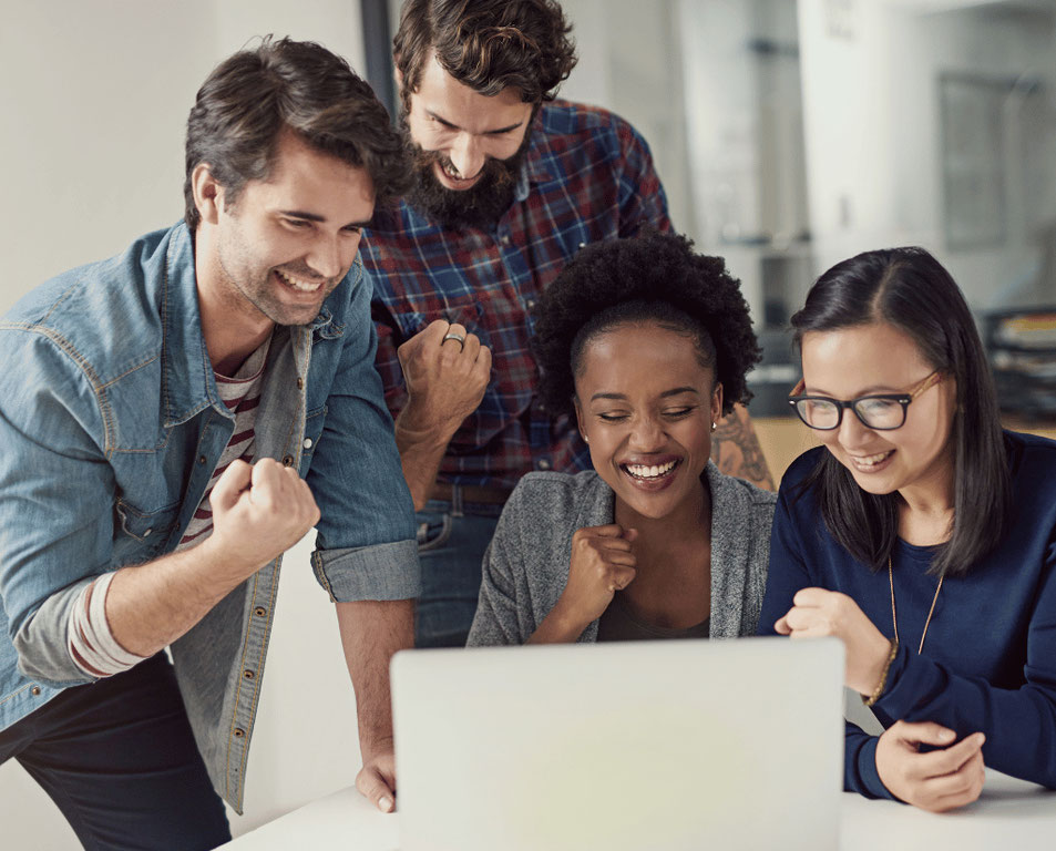 Two men standing and two women sitting facing an open laptop computer on a desk, they are all fist-pumping to depict they just benefited from what is happening on the computer screen.