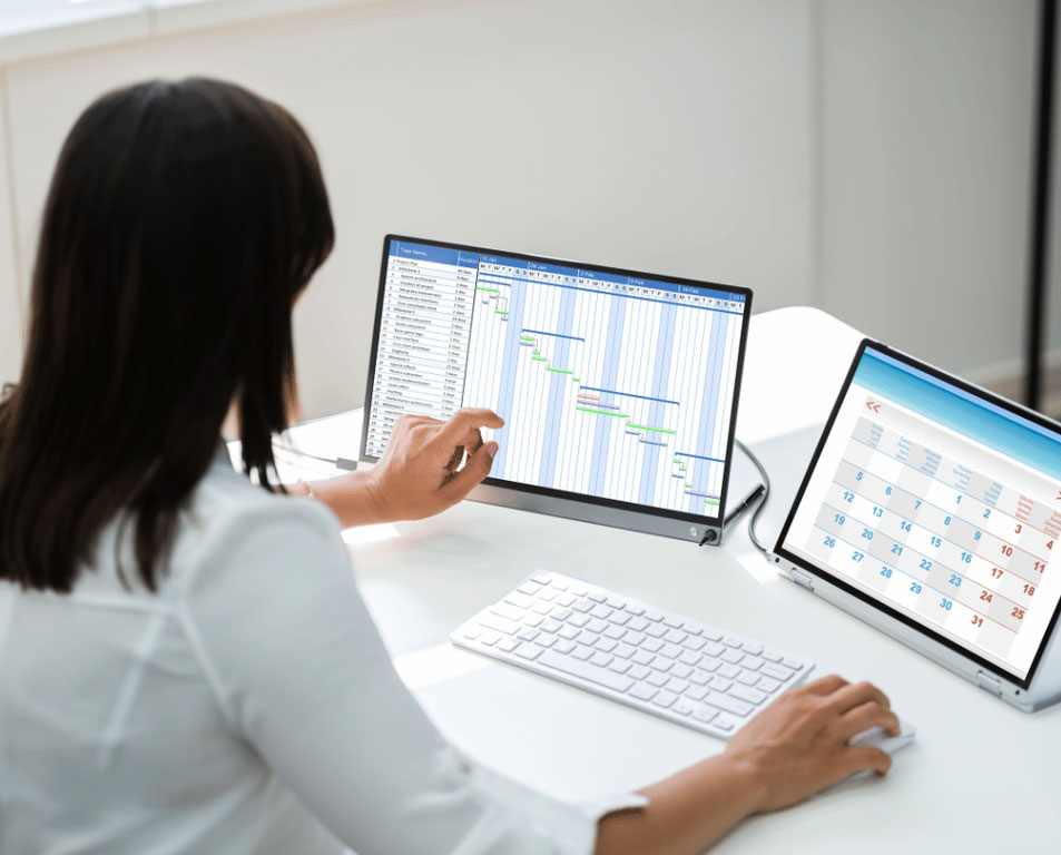 A person sitting at a desk with two computer screens and a keyboard depicting the use of multiple tools and technology